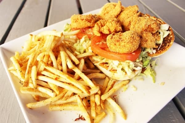 The Shrimp Po’Boy features fried shrimp atop a bed of lettuce and tomatoes, served on a hoagie with a side of fries.