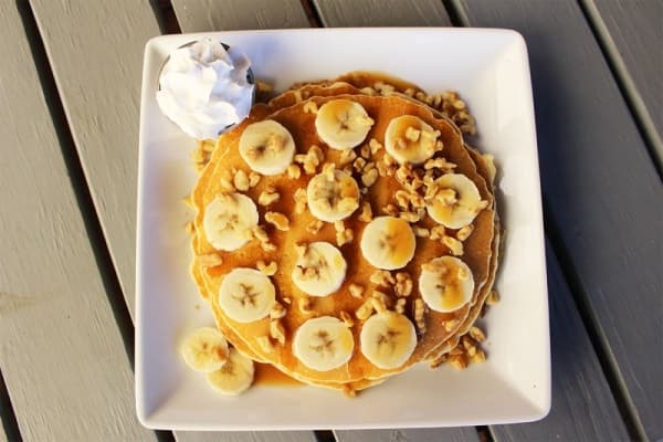 The caramel banana pancakes include two pancakes topped with fresh banana slices, walnuts and a caramel drizzle, served with whipped cream and a side of bacon, sausage or chicken sausage.