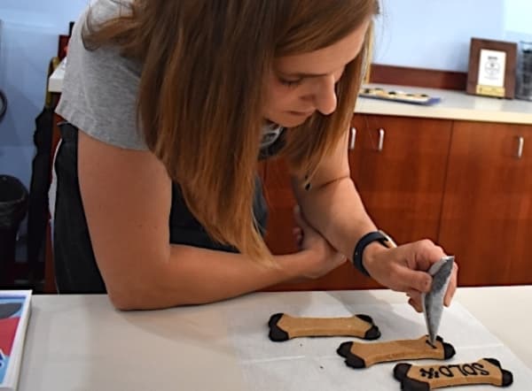 Co-owner Carin Giga personalizes a few treats using carob, a dog-friendly chocolate substitute, to write the names of the customer's dogs. (Alex Hosey/Community Impact Newspaper)