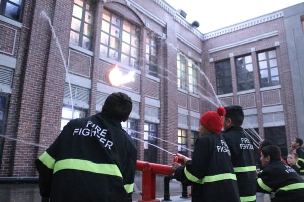 Children training to be firefighters extinguish a fire at a building.