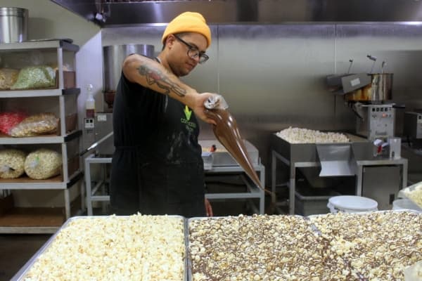 Flavor technician Warren Crosley drizzles chocolate over kettle corn to create the dark chocolate-peanut butter combo. (Amy Denney/Community Impact Newspaper)