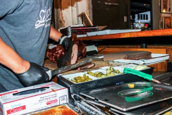 Stiles Switch General Manager Duane Jackson slices brisket behind the counter. It is smoked in oak and coated with black pepper. Emma Freer/Community Impact Newspaper