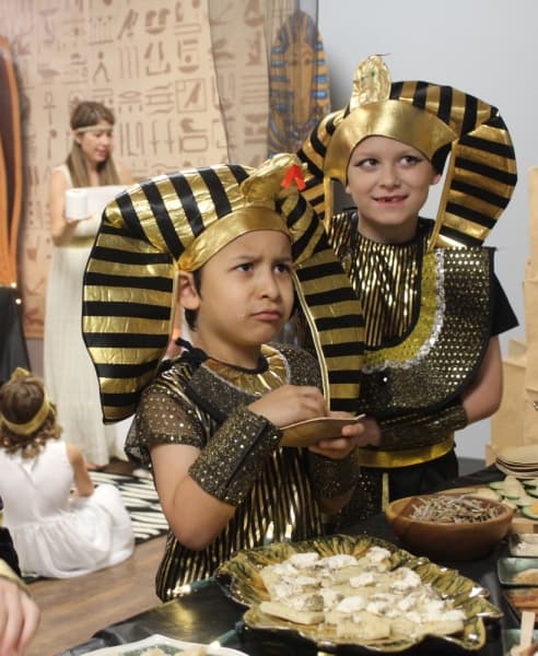 First graders Blake Adelsman and Joaquin Lopez react to an explanation of the ancient Egyptian diet during the private school's Egyptian feast on Nov. 19.  (Brian Perdue, Community Impact Newspaper)