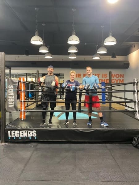 A photo of three adults wearing boxing gloves and smiling in a boxing ring.