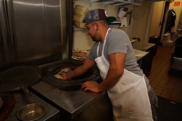 A cook places dough along the inner clay walls of the charcoal-fired tandoor oven.