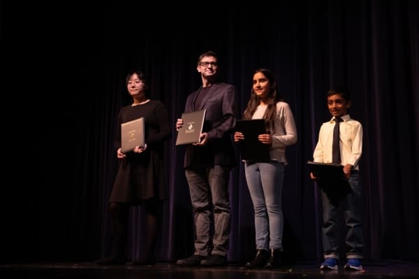 Art finalists in the Plano ISD Proud competition are presented awards on stage. Hallie Wang, Rice Middle School student, was recognized as the contest winner. (Left to right: Hallie Wang; Colin McGrane, stand in for Tristan Talkington; Noa Rotem; and Pranav Balakrishnan) (Liesbeth Powers/Community Impact Newspaper)