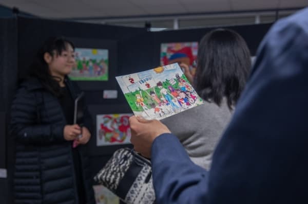 Hallie Wang, Rice Middle School student, poses next to her winning piece. A family member of hers looks at a print out of the work while she takes photos to commemorate the win. (Liesbeth Poweers/Community Impact Newspaper)