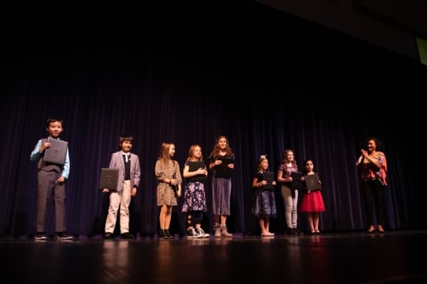 Winners of the writing contest stand on stage with their awards. (Left to right: Alex Zhu, Timothy Wenick, Mila Sanders, Amelia Roy, Lillian Pitluk, Taylor Nguyen, Eiley Moilanen, Marillany Alcantar) (Liesbeth Powers/Community Impact Newspaper)
