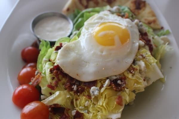 The crowned wedge salad is priced at $9.99 and includes blue cheese crumbles, sugar curbed bacon and a fried egg. (Amy Rae Dadamo/Community Impact Newspaper) 