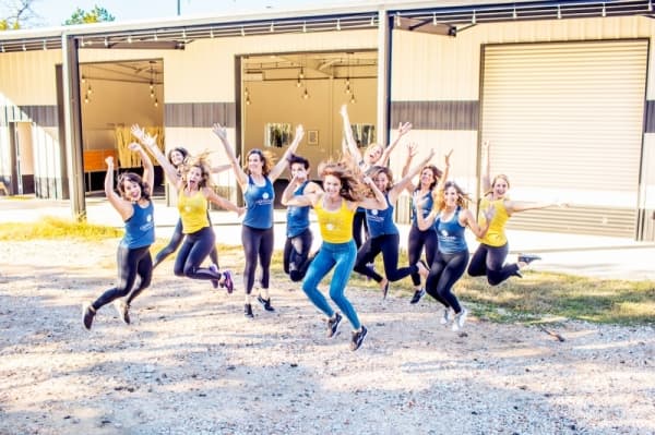 A photo of a group of women in yellow and blue fitness gear leaping into the air in celebration.