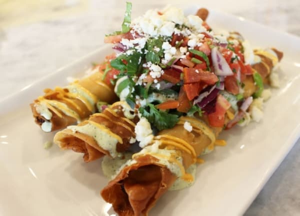 Breakfast Taquitos ($10.99) are made with chicken and cheese in deep-fried flour tortillas and topped with onions, cilantro, tomatoes, avocado, queso fresco, avocado ranch sauce, jalapenos and chili powder.