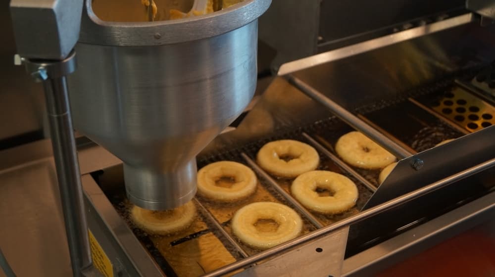 Freshly prepared dough is transferred from the doughnut mixer onto a conveyor belt to be properly fried and cooked. (Kelsey Thompson/Community Impact Newspaper)
