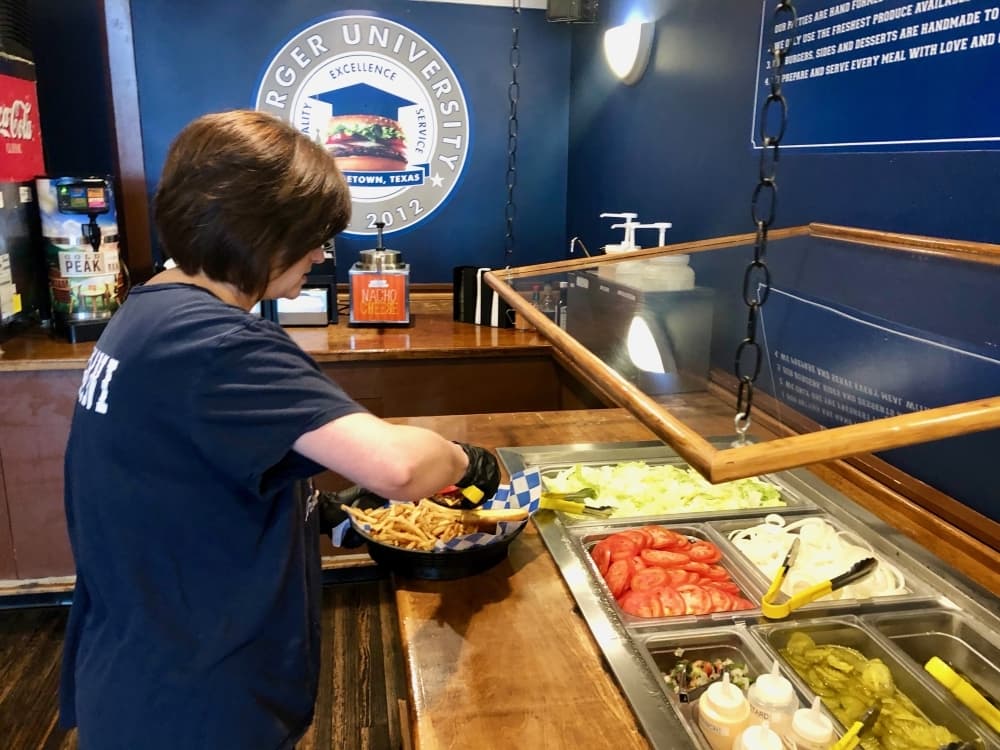 Burger University owner Carmen May puts a salad together for a customer March 16 to avoid an unnecessary amount of people at the salad bar. (Sally Grace Holtgrieve/Community Impact Newspaper)