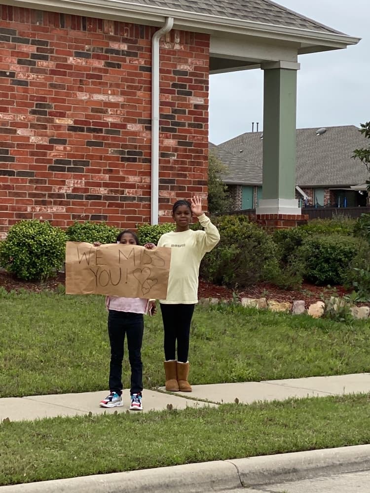 Two students along the car parade route hold a "We Miss You!" sign. (Courtesy Kyla Prusak)