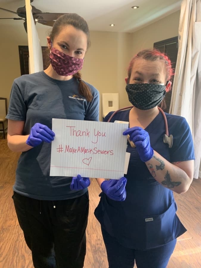A photo of two medical workers wearing hand-sewn masks and holding a sign that reads "Thank you #MakeAMask sewers."