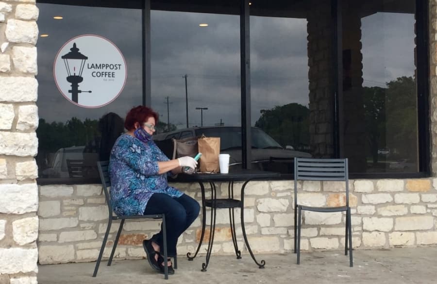 A woman wearing a cloth mask and latex gloves sits in front of Lamppost Coffee in Round Rock. (Taylor Jackson Buchanan/Community Impact Newspaper)