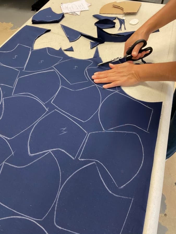 A photo of masks being cut out of blue fabric