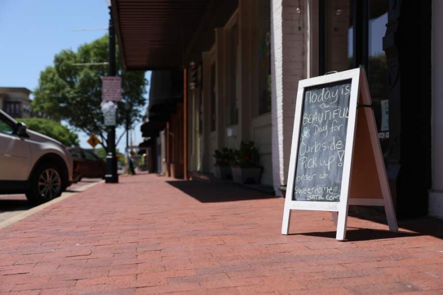 Signs encouraging customers to use curbside retail are placed in windows and in front of stores in downtown Plano. In front of Sweet Home Bath + Body, a sign reads, "Today is a beautiful day for curbside pickup!" (Liesbeth Powers/Community Impact Newspaper)