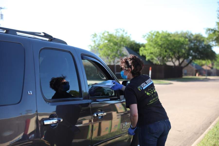 Cornelia Datcu brings dental kits for basic dental hygiene to the window of a car during the free meals and testing event in Allen. (Liesbeth Powers/Community Impact Newspaper)