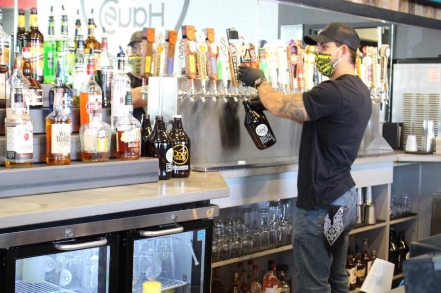 A masked employee pours beer into a growler at Dog Haus Biergarten, which reopened its dining room at 25% capacity May 1. (Olivia Lueckemeyer/Community Impact Newspaper)