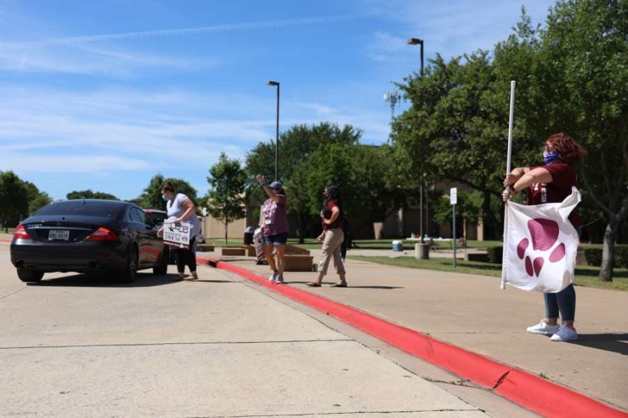 Seniors are welcomed into the parking lot by flag twirler Erin Walker, a special education teacher at Plano Senior High School. Yard signs are then placed in the cars of seniors and their families. (Liesbeth Powers/Community Impact Newspaper)