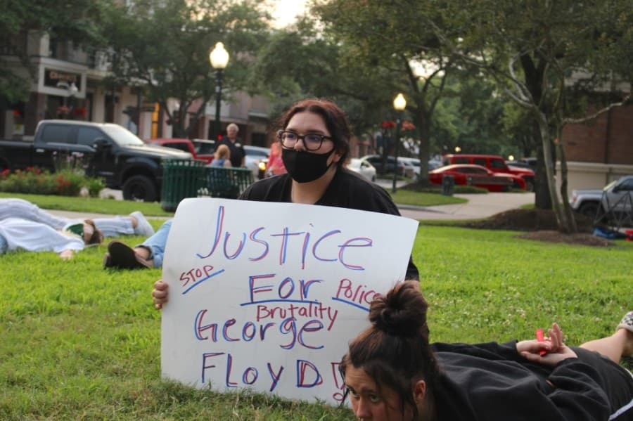Protesters hold handmade signs while they sit and lay on the grass of Town Center Park on June 1. (Kelly Schafler/Community Impact Newspaper)
