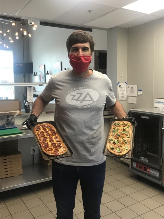'Zza co-owner Ryan McManus stands with a pepperoni pizza, $9, on the left and a Thai Dye pizza, $10, which are two of the restaurant's more popular items. (Amy Rae Dadamo/Community Impact Newspaper) 