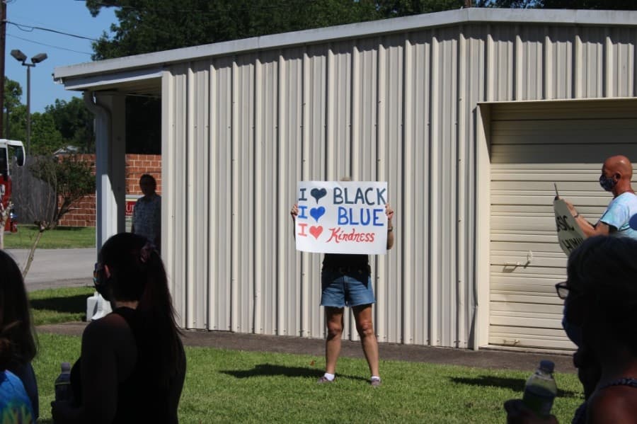 A community member holds a sign at the corner of Malone and South Pine streets as the group of protesters passes by. (Dylan Sherman/Community Impact Newspaper)