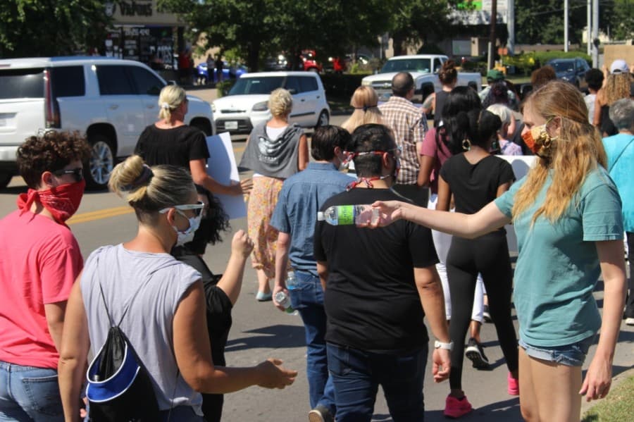 A community member hands water bottles to protesters as they pass by on West Main Street on June 13. (Dylan Sherman/Community Impact Newspaper)