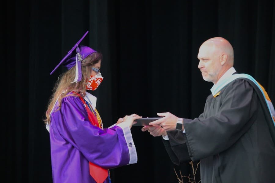 Superintendent Tim Harkrider gives a diploma to a masked graduate. (Andy Li/Community Impact Newspaper)