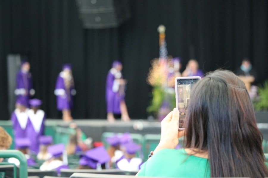 A guest takes photos as graduates walk across the stage. (Andy Li/Community Impact Newspaper)