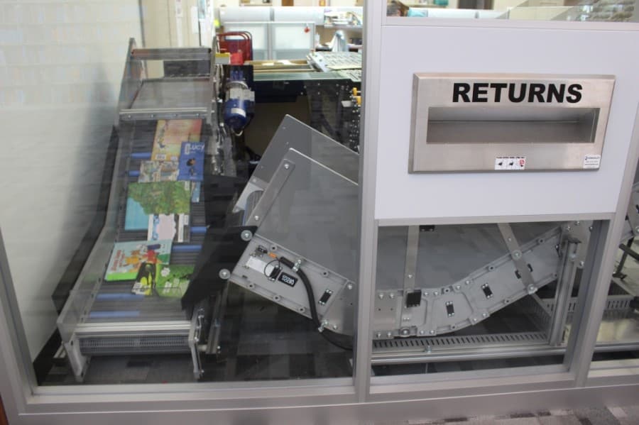 Due to the usually high circulation at the library, an automated material handler was installed to help sort books faster. Books or other library items are deposited onto a conveyor belt, which sorts them individually and scans the item in. From there, items move along the conveyor belt and are dropped in the correct container for each section, which staff will distribute. (Miranda Jaimes/Community Impact Newspaper)