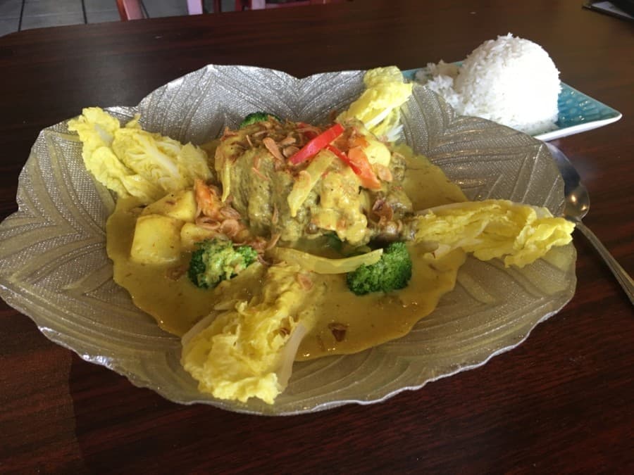 Oxtail stew is served in a yellow curry sauce with steamed baby bok choy and white jasmine rice, topped with crispy fried onion. (Shawn Arrajj/Community Impact Newspaper)