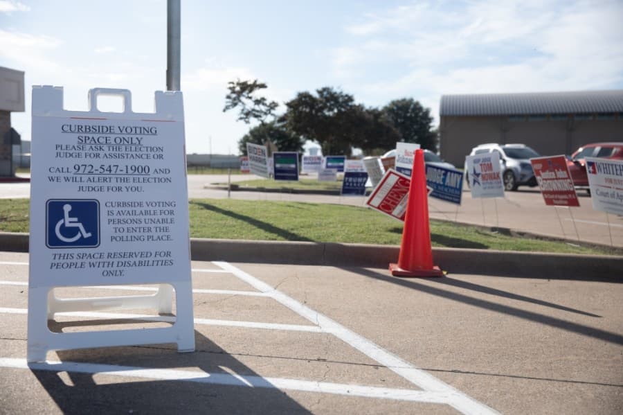 Parking spaces marked for curbside voting include a sign with instructions for voters to call for assistance. (Liesbeth Powers/Community Impact Newspaper)