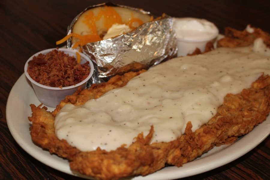 The large chicken-fried steak with gravy ($15.95) is served with a baked potato. (Eva Vigh/Community Impact Newspaper)