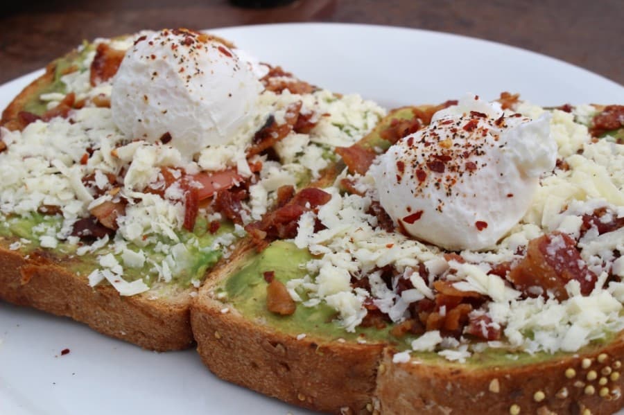 The Breakfast Club's avocado toast ($8.99) includes two slices of multgrain bread topped with avocado, sliced tomato, eggs, cotija cheese, crumbled bacon, and crushed red pepper. (Ben Thompson/Community Impact Newspaper)