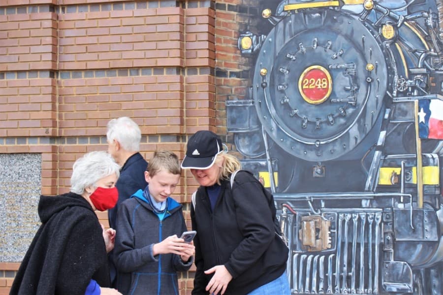 Guests took turns snapping photos in front of the train mural on the outside of the station on April 24. (Sandra Sadek/Community Impact Newspaper)