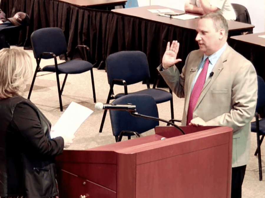 Mike Lombardo with his hand up as he is sworn in.