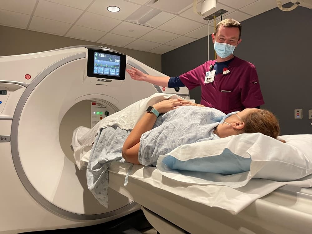 hospital employee standing with patient going into a CT scanner 