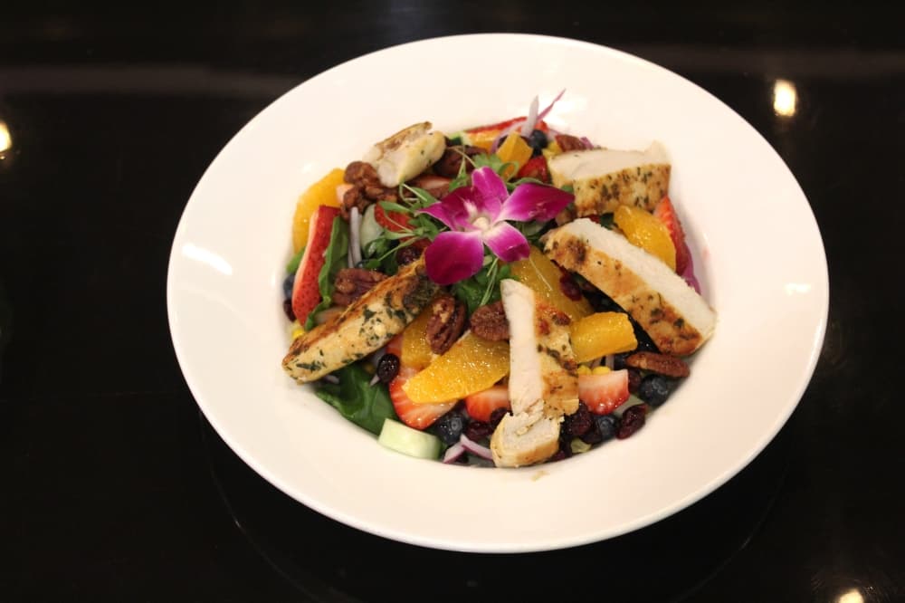 Spinach salad with chicken ($20): Grilled chicken, cherry tomatoes, apples, red onion and candied pecans are served in a dijon honey mustard. (Savannah Kucher/Community Impact Newspaper)