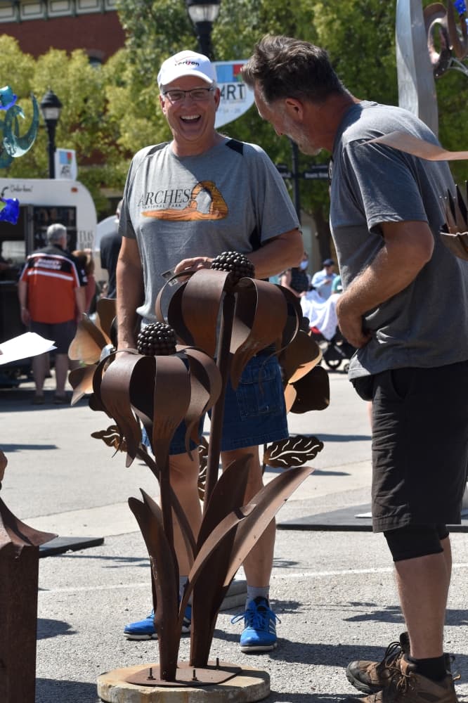 two men talk alongside a metal sculpture 