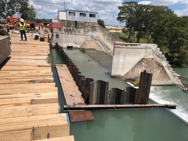 Workers use a temporary trestle bridge to work on the dam. (Courtesy Guadalupe-Blanco River Authority, Zachary Construction Corp.)