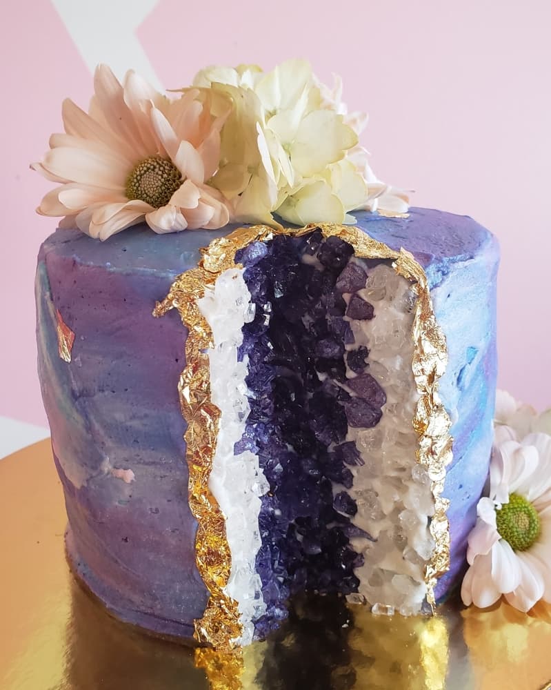 This custom geode cake has a marble cake base with vanilla buttercream, rock candy geode, edible gold leaf and fresh flowers. (Courtesy Scrumptious Houston)