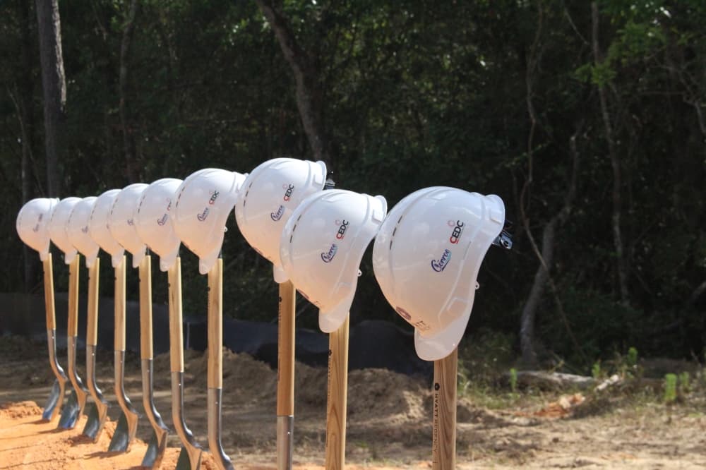 A line of white hard hats on shovels planted into the soil