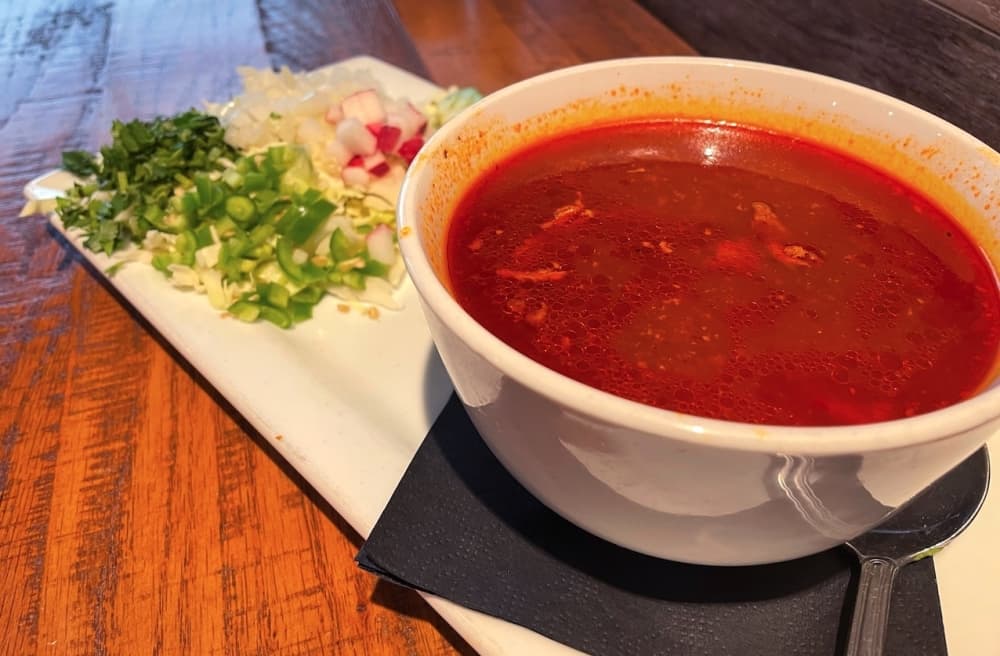 Pozole is a spicy, traditional Mexican soup that is made from hominy, pork, chili peppers, jalapenos and oregano. It is served with serranos, cabbage, onions, radishes and cilantro. (Sandra Sadek/Community Impact Newspaper)