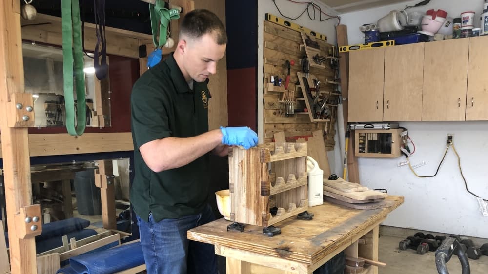 Szabo applies finish to a zebra wood wine bottle holder, a project completed with only the use of hand tools, as requested by the customer. (Grace Dickens/Community Impact Newspaper)