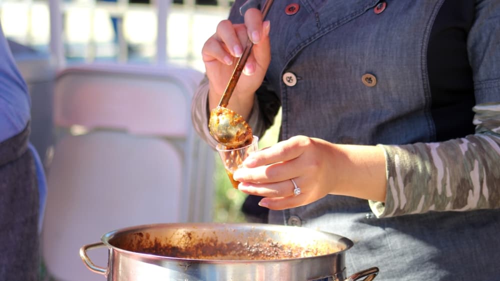 A woman serves chili in a cup.