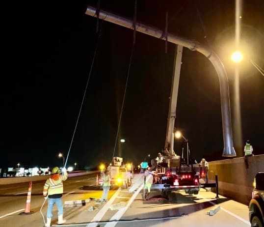 Crews placing pole for sign on highway at night