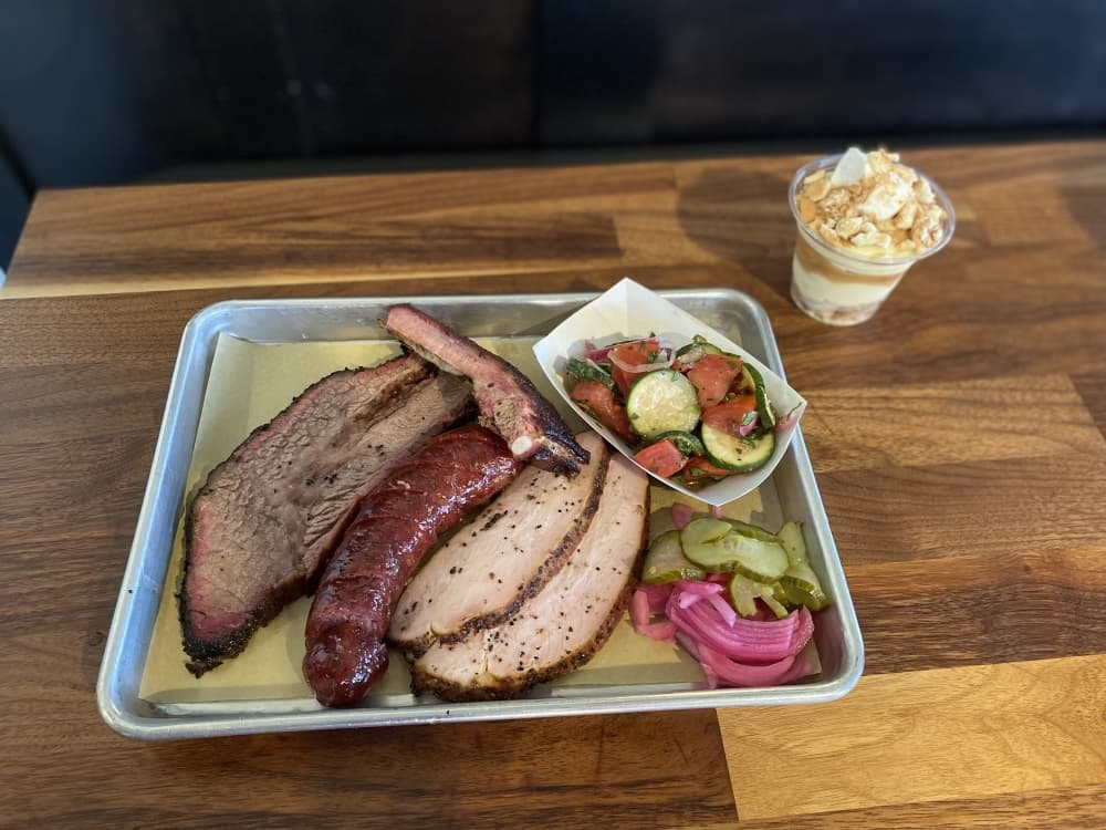 A platter of meats includes Angus beef prime brisket ($15), beef kielbasa ($6), pork rib ($11.50) and turkey breast ($10) as well as sides such as a tomato zucchini salad ($3.50). (Trent Thompson/Community Impact Newspaper)