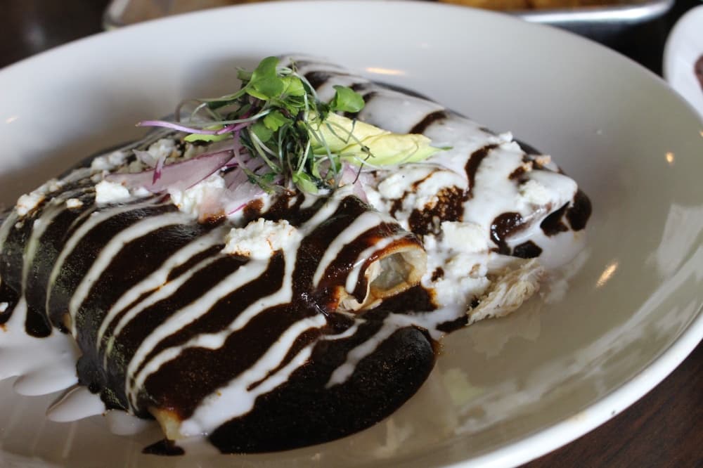 The enchiladas de mole ($16) is shredded chicken breast rolled in three corn tortillas smothered in mole and served over black bean purée topped with toasted sesame seeds, onion and crema Mexicana. (Ally Bolender/Community Impact Newspaper)